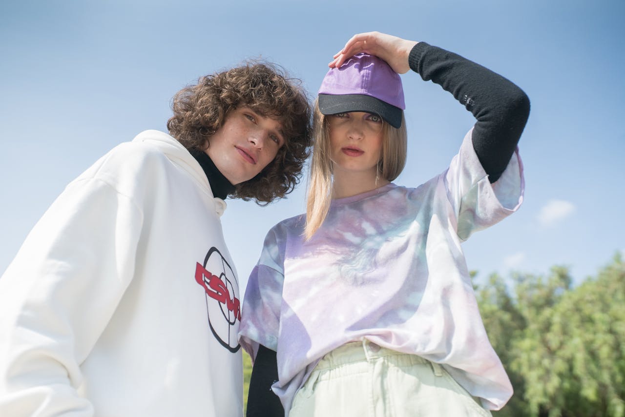Young couple posing in colorful streetwear fashion, showcasing casual style with caps and hoodies outdoors.